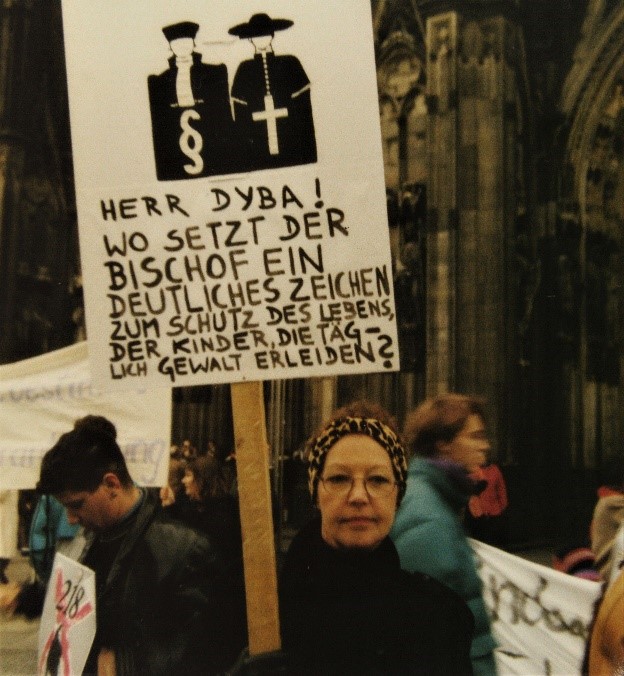 Inge von Bönninghausen bei Demonstration zum Paragraph 218 am Kölner Dom, 1990. Sie trägt ein Schild mit der Aufschrift: „Herr Dyba! Wo setzt der Bischof ein deutliches Zeichen zum Schutz des Lebens der Kinder, die täglich Gewalt erleide?“.